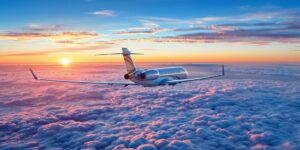 Large private jet flying above clouds at sunset.